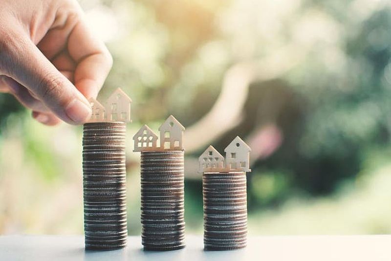 Cropped hand putting model homes on stacked coins